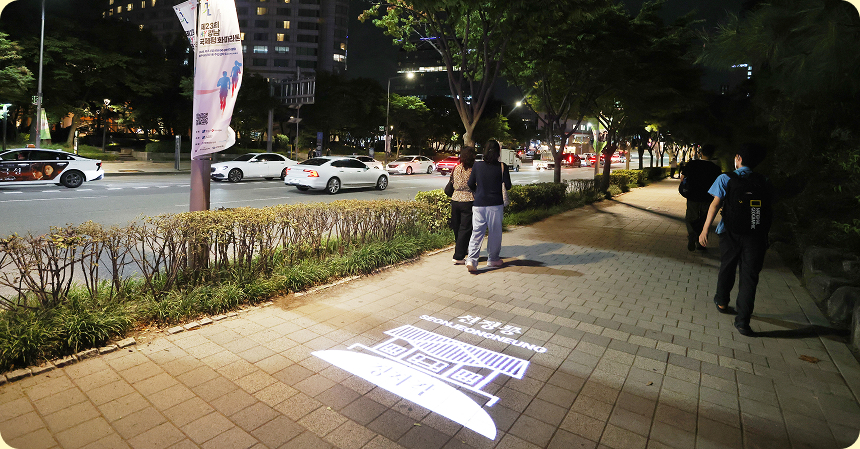 야간 보행로 바닥에 미디어 조명이 투사되고 있는 은은한 빛의 역사문화거리 전경